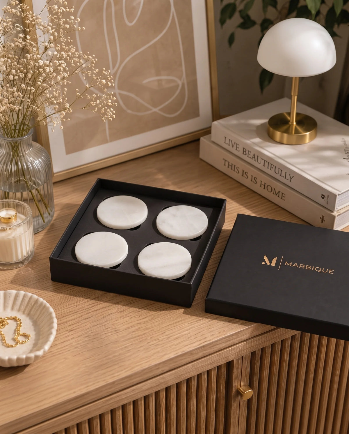 Plain white round coasters with subtle veining in a black Marbique box on a wooden cabinet.