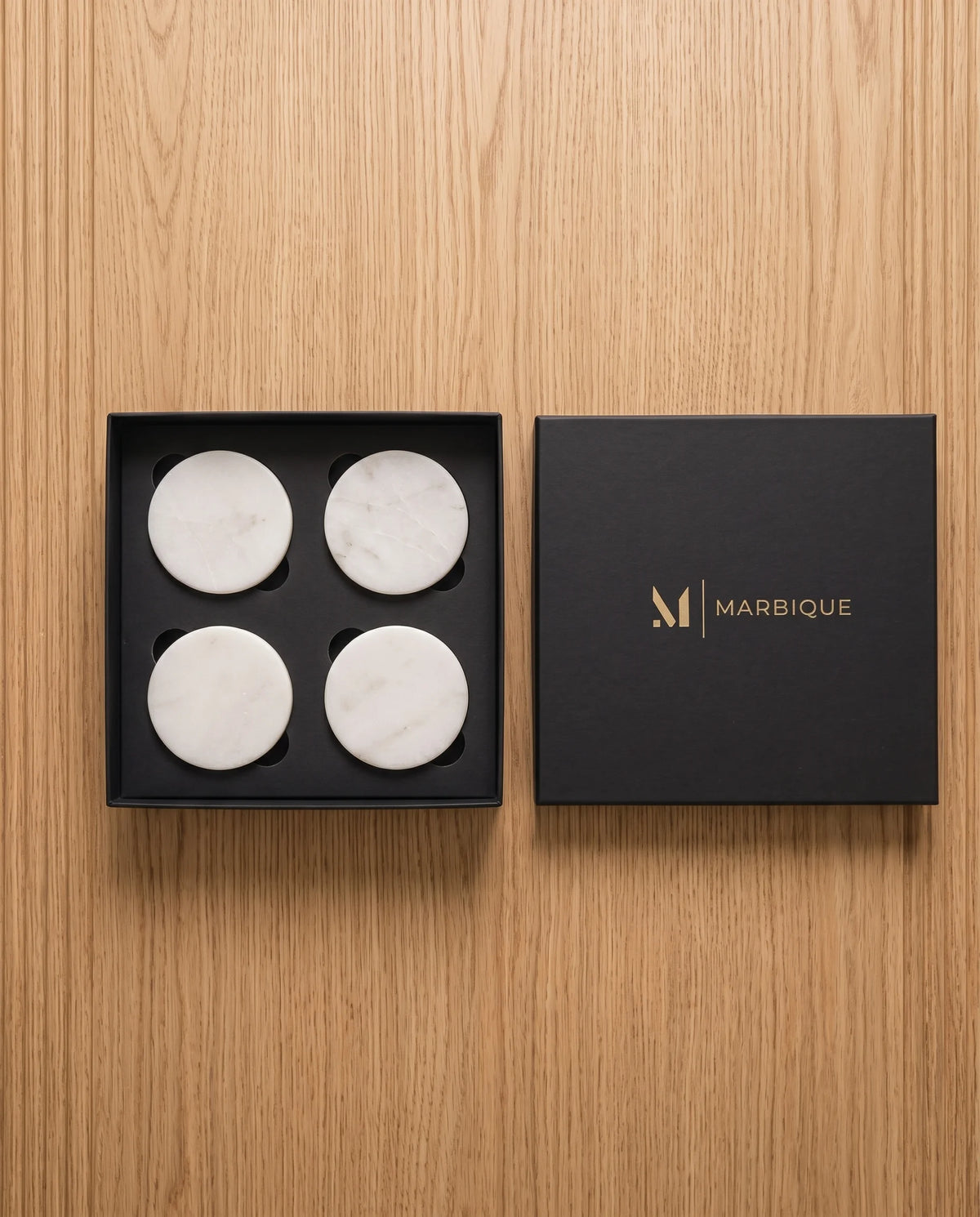 White round coaster designs photographed beside black Marbique presentation packaging.