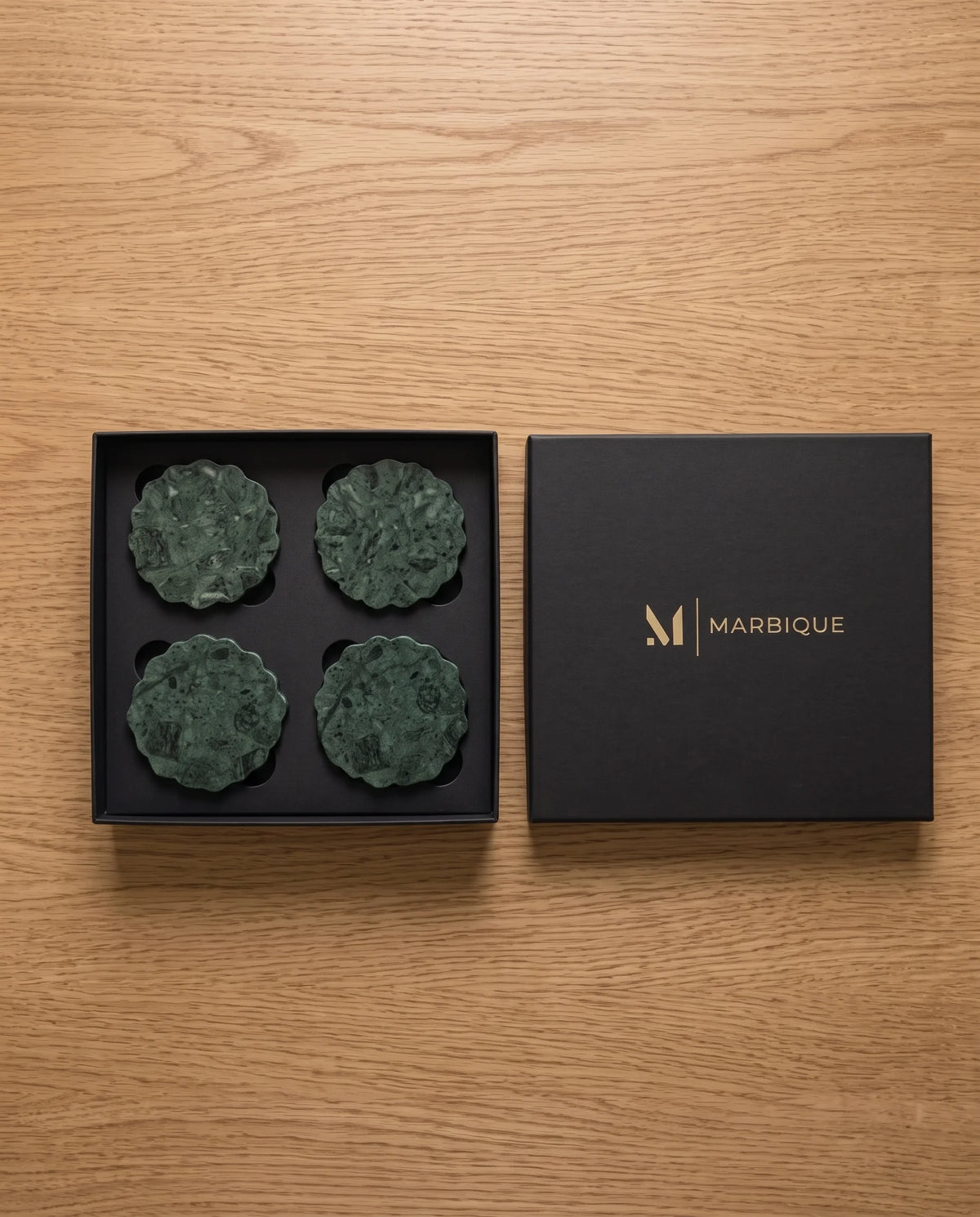 Dark green scalloped round coasters with mottled surfaces arranged in a black Marbique box.