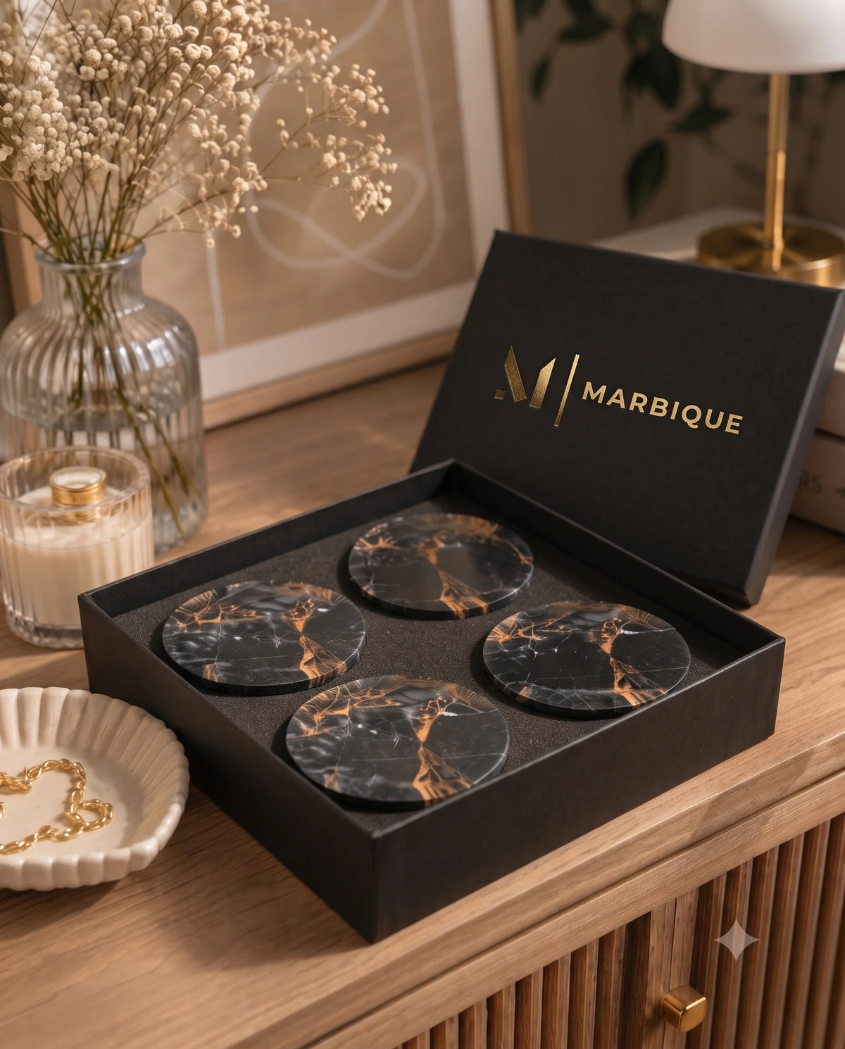 Black round coasters with warm gold-tone and pale veining in an open black Marbique box.
