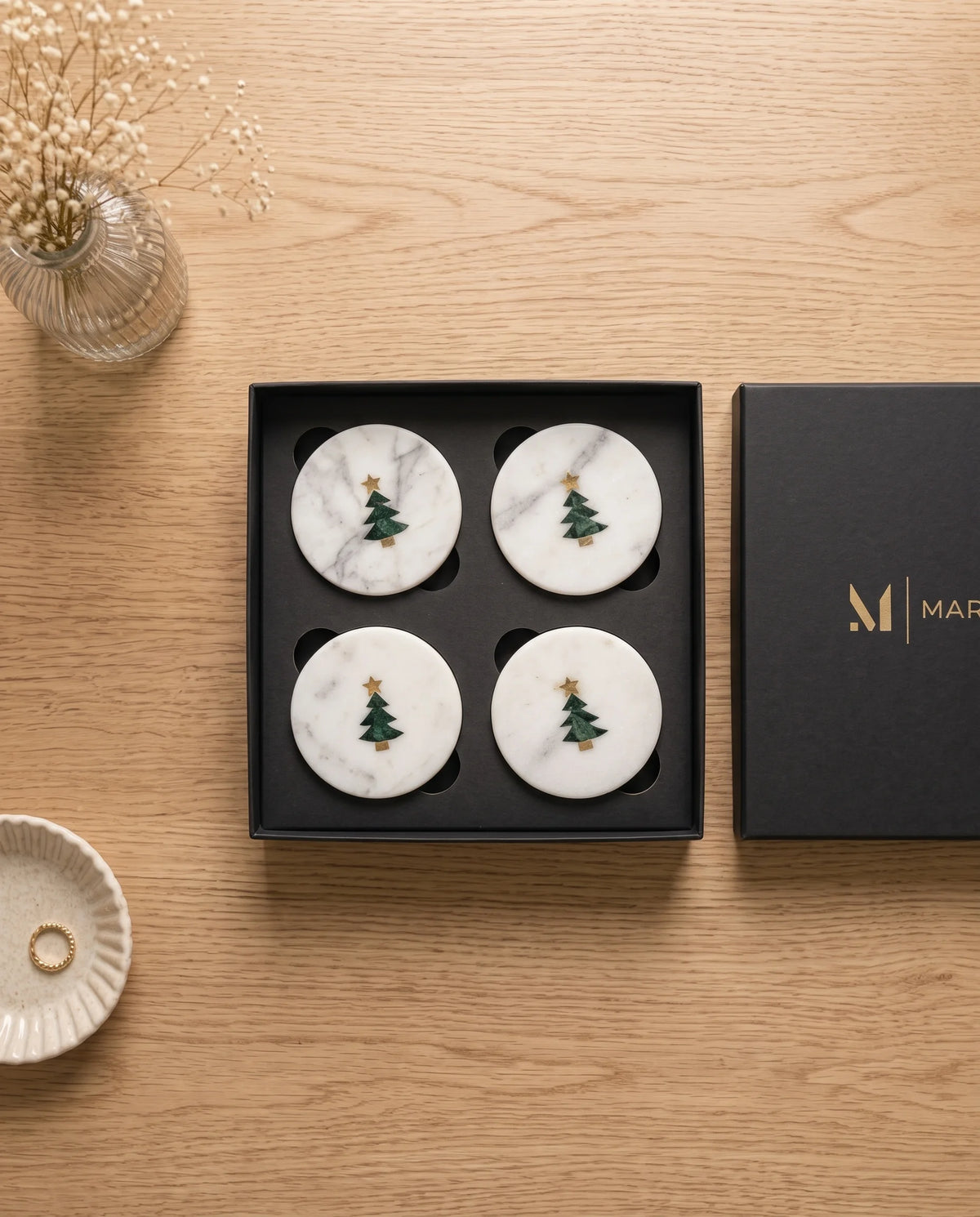 White circular Christmas tree coasters displayed beside black presentation packaging.