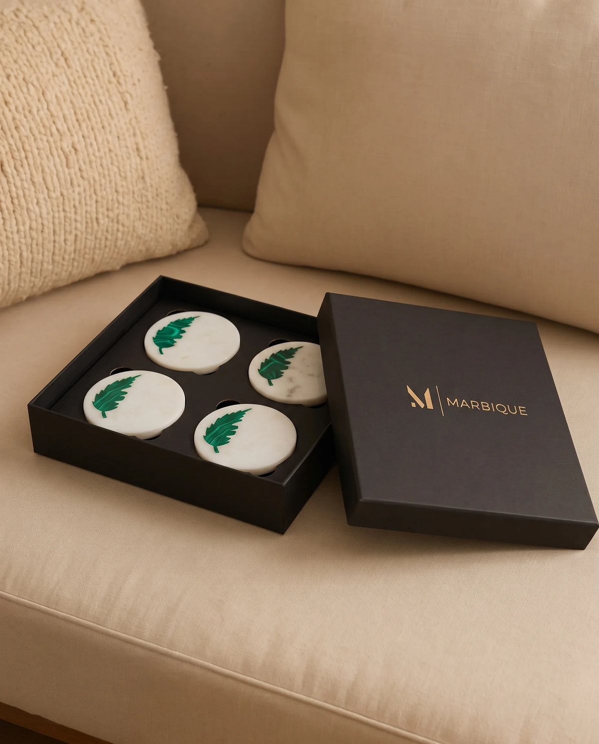 White round coasters with green leaf motifs arranged in a black Marbique presentation box.