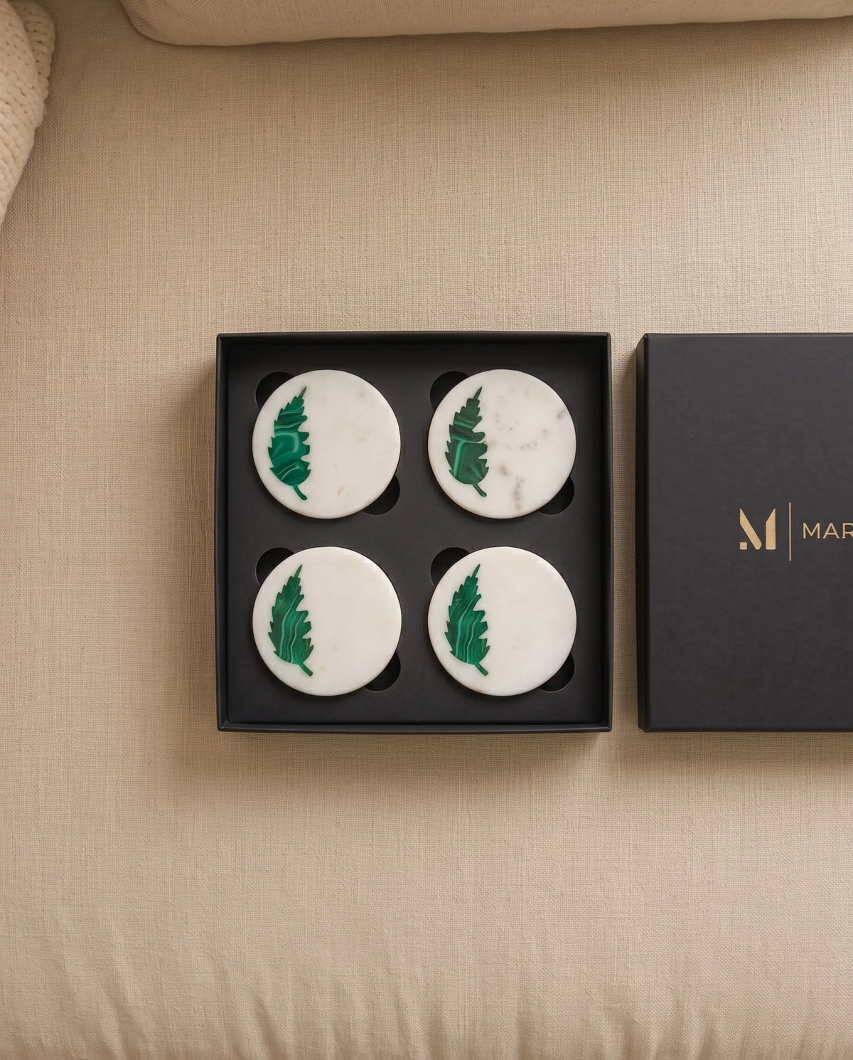 White round leaf-motif coasters photographed with black presentation packaging.