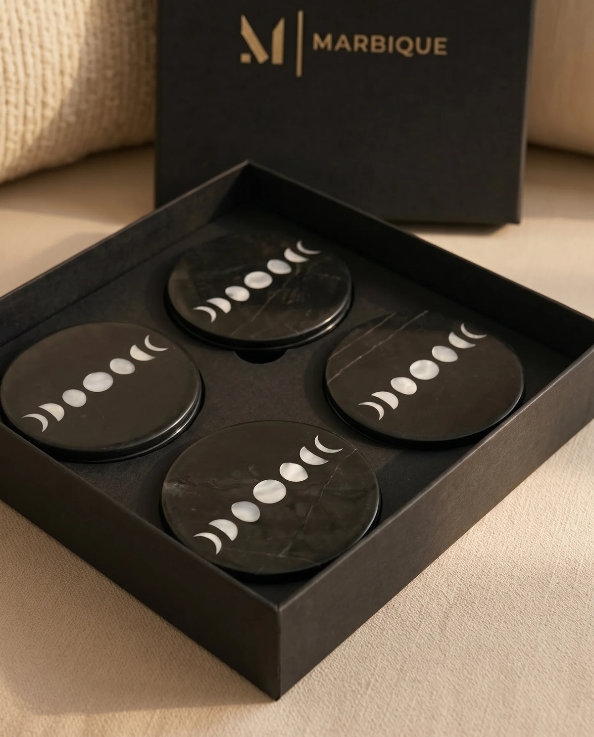 Black moon-phase coaster designs photographed with Marbique presentation packaging.