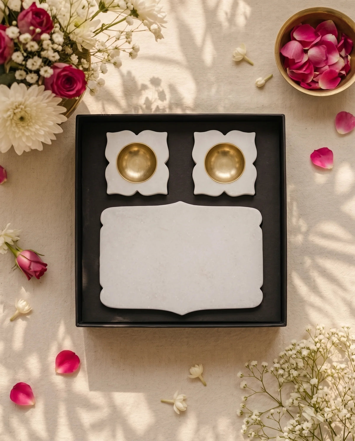 Open black box displaying a plain white shaped rectangular tray and two floral diya holders with gold-tone cups.