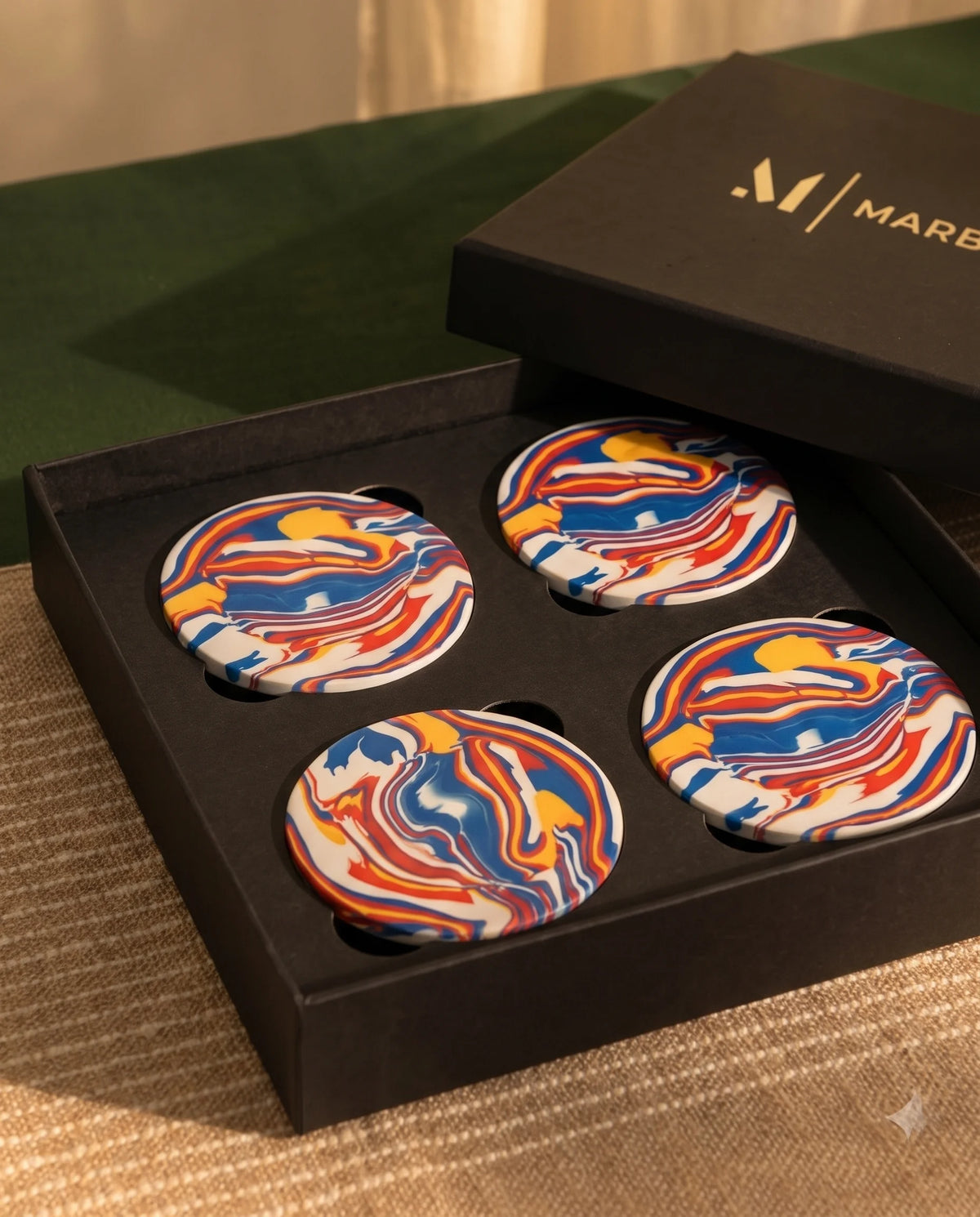 Multicolour round coasters with blue, red, yellow and white swirl patterns arranged in a black Marbique box.