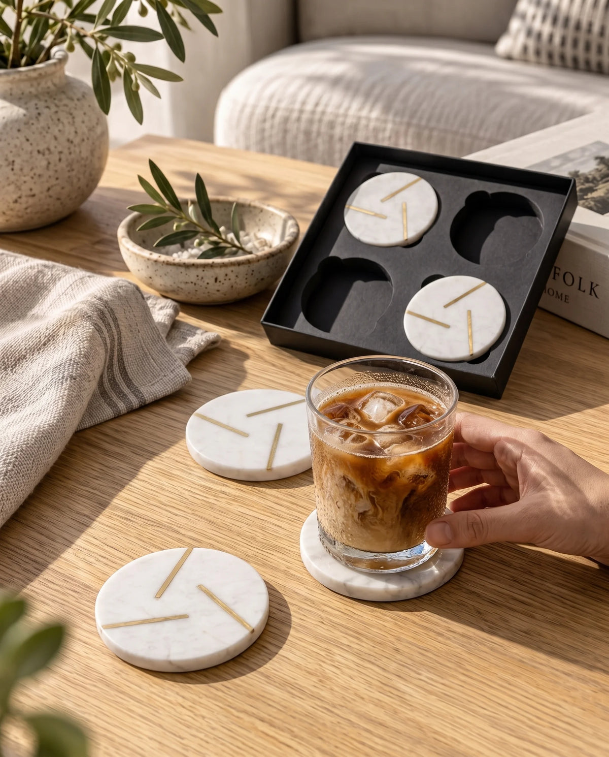 White round coasters with intersecting gold-tone lines arranged in a black Marbique box beside a matching coaster.