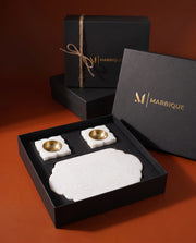 White oblong tray with scalloped ends and two petal-shaped gold-tone-cup holders inside black Marbique packaging.