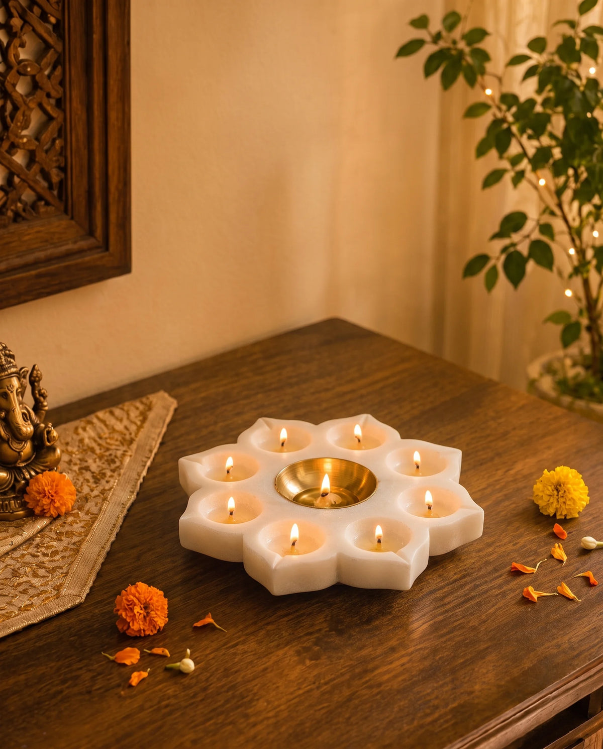 White flower-shaped holder with lit candles in petal recesses and a gold-tone central cup on a wooden altar.