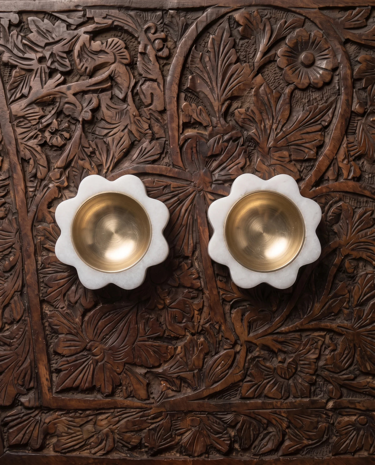 Overhead view of two white rounded-flower diya holders with circular gold-tone cups.