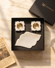 White pointed scalloped tray and two four-petal holders with gold-tone cups in an open black box.