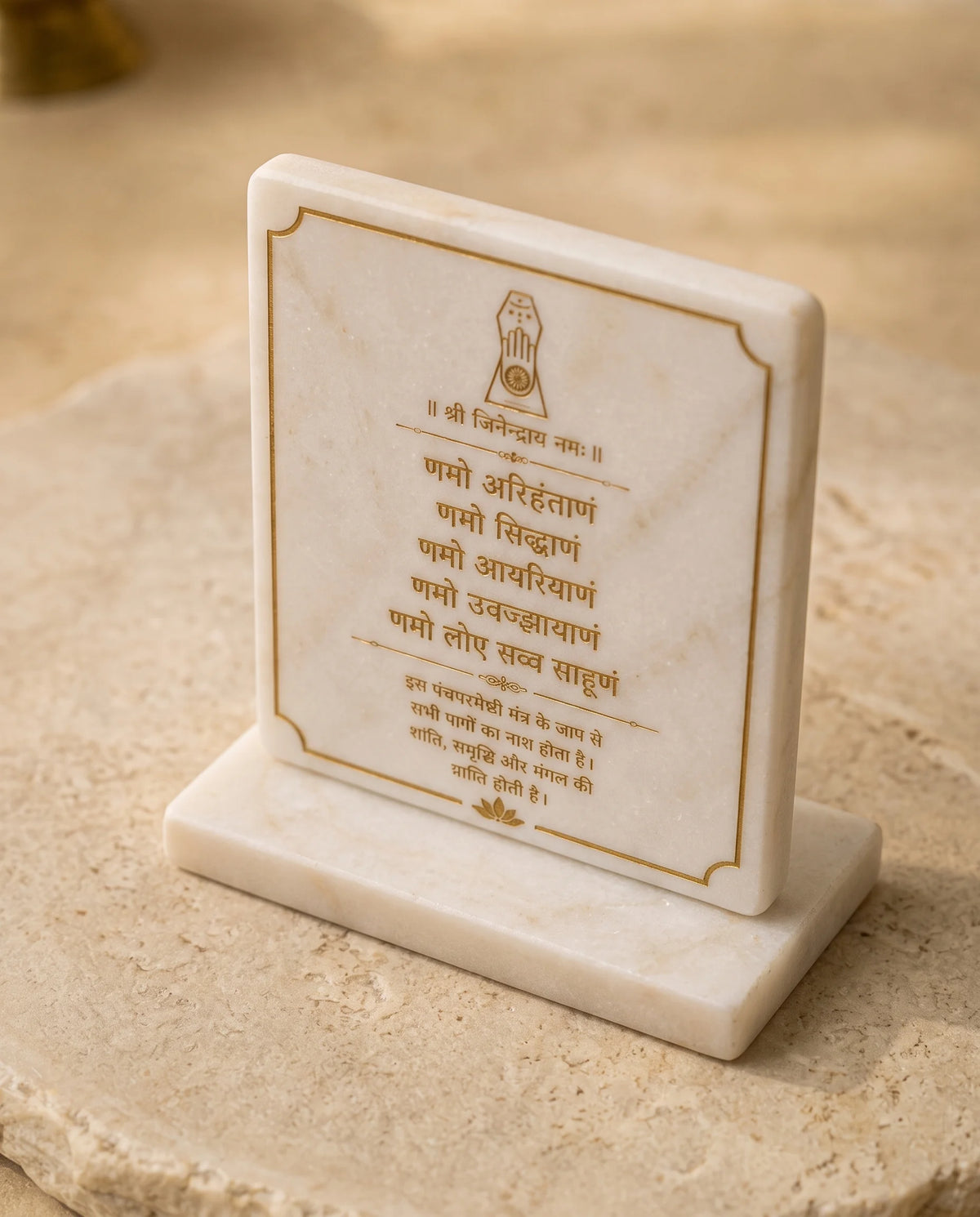 White Namokar Mantra plaque with gold-tone Devanagari lettering and a Jain hand symbol, pictured upright on a rectangular base.