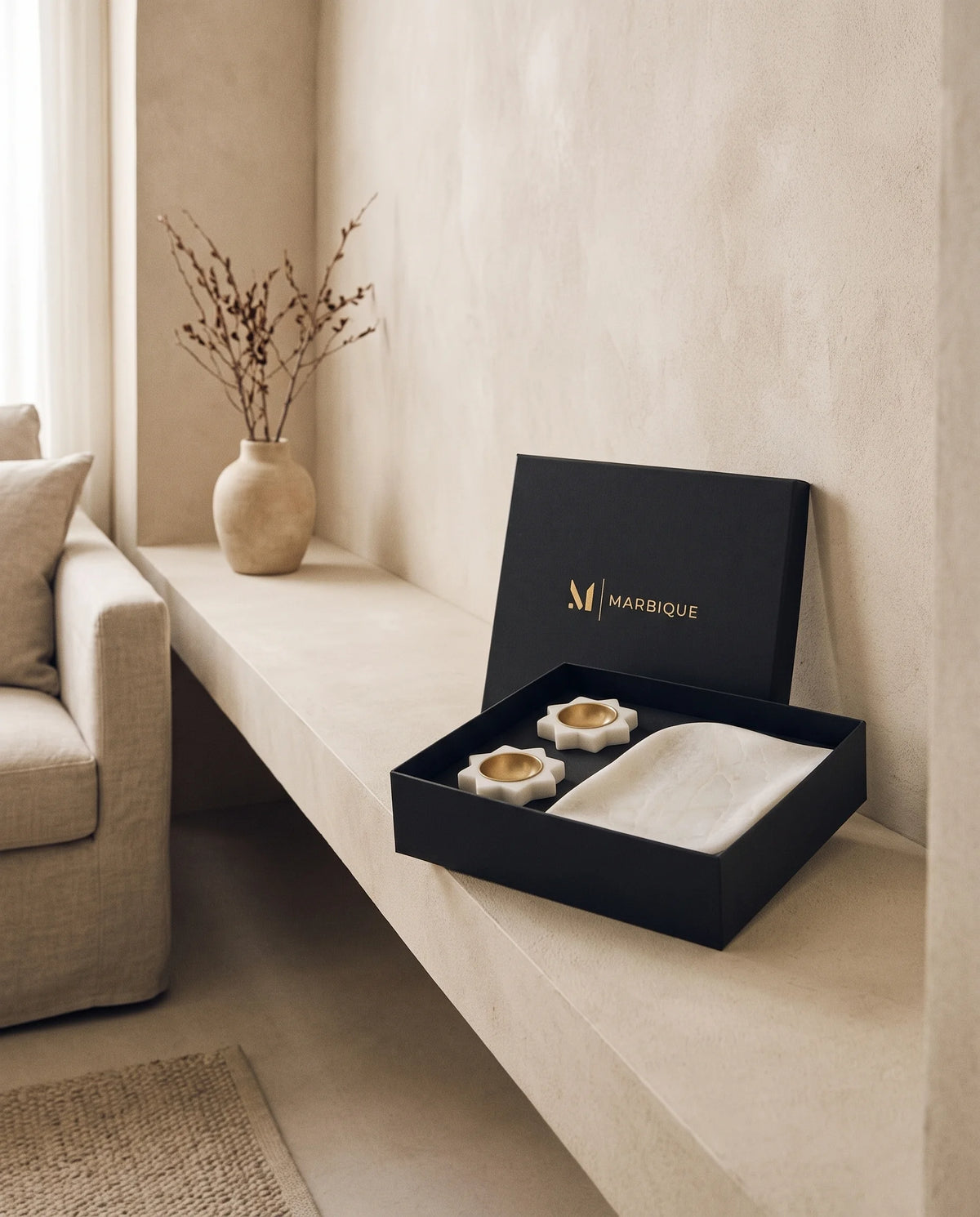 White scalloped rectangular tray and two floral gold-tone-cup holders in a black box on a light shelf.