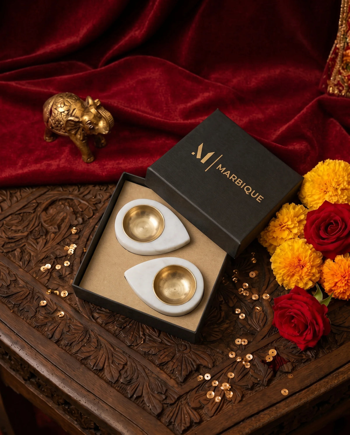 Two white teardrop diya holders with round gold-tone cups, viewed from above on a carved table.
