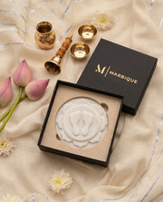 White circular pooja plaque with raised footprints, a layered floral motif and soft grey veining.