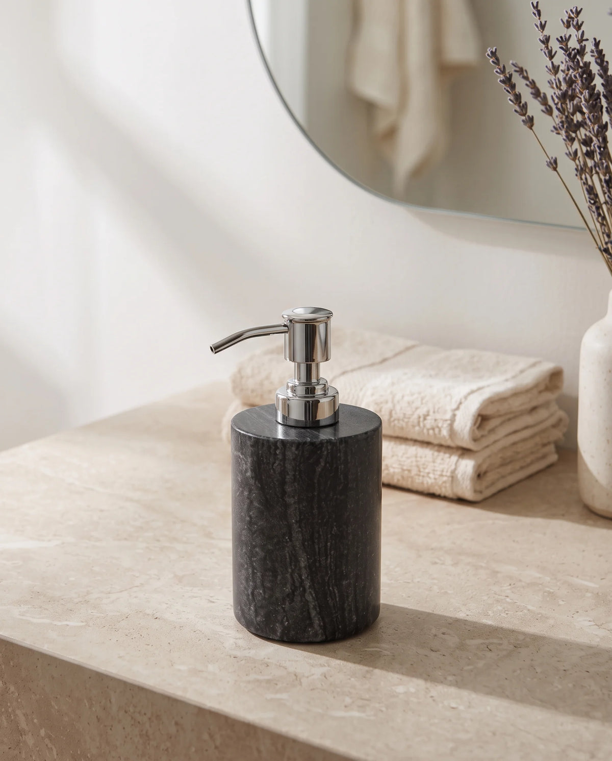 Charcoal cylindrical bathroom dispenser with pale veining and a silver-tone pump beside folded towels.