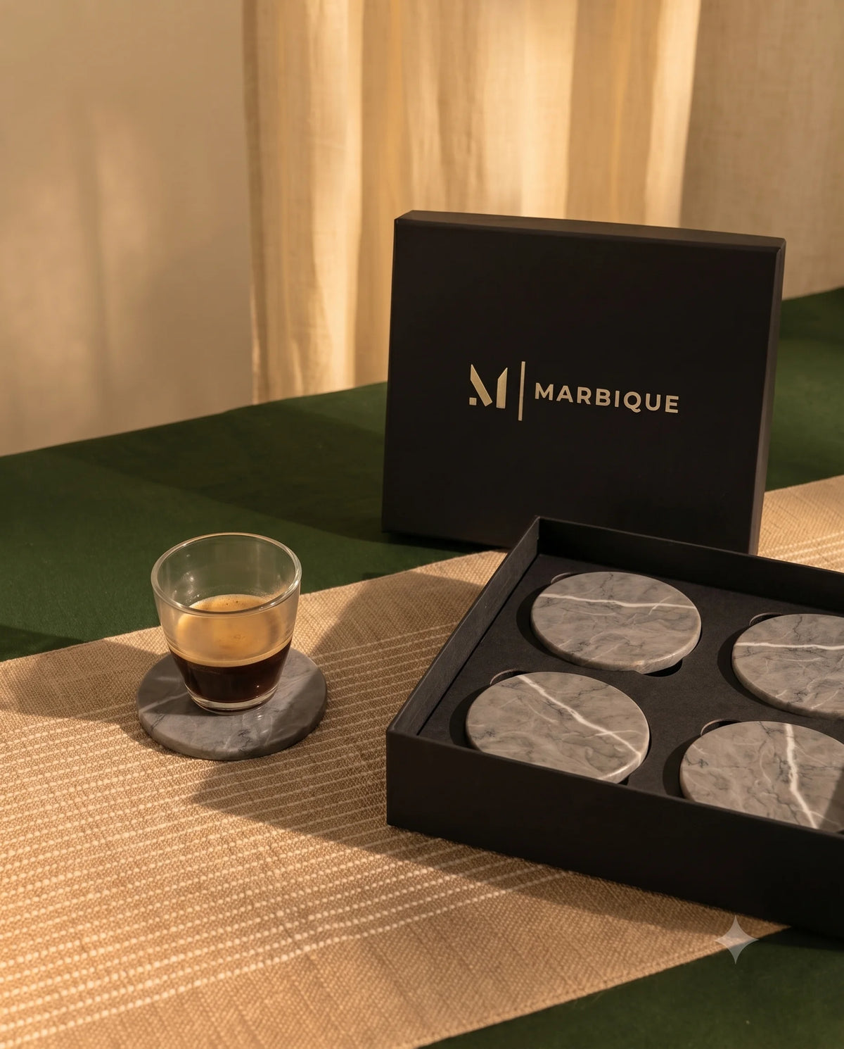 Grey round coasters with pale veining in a black Marbique box, with an espresso glass on another coaster beside it.