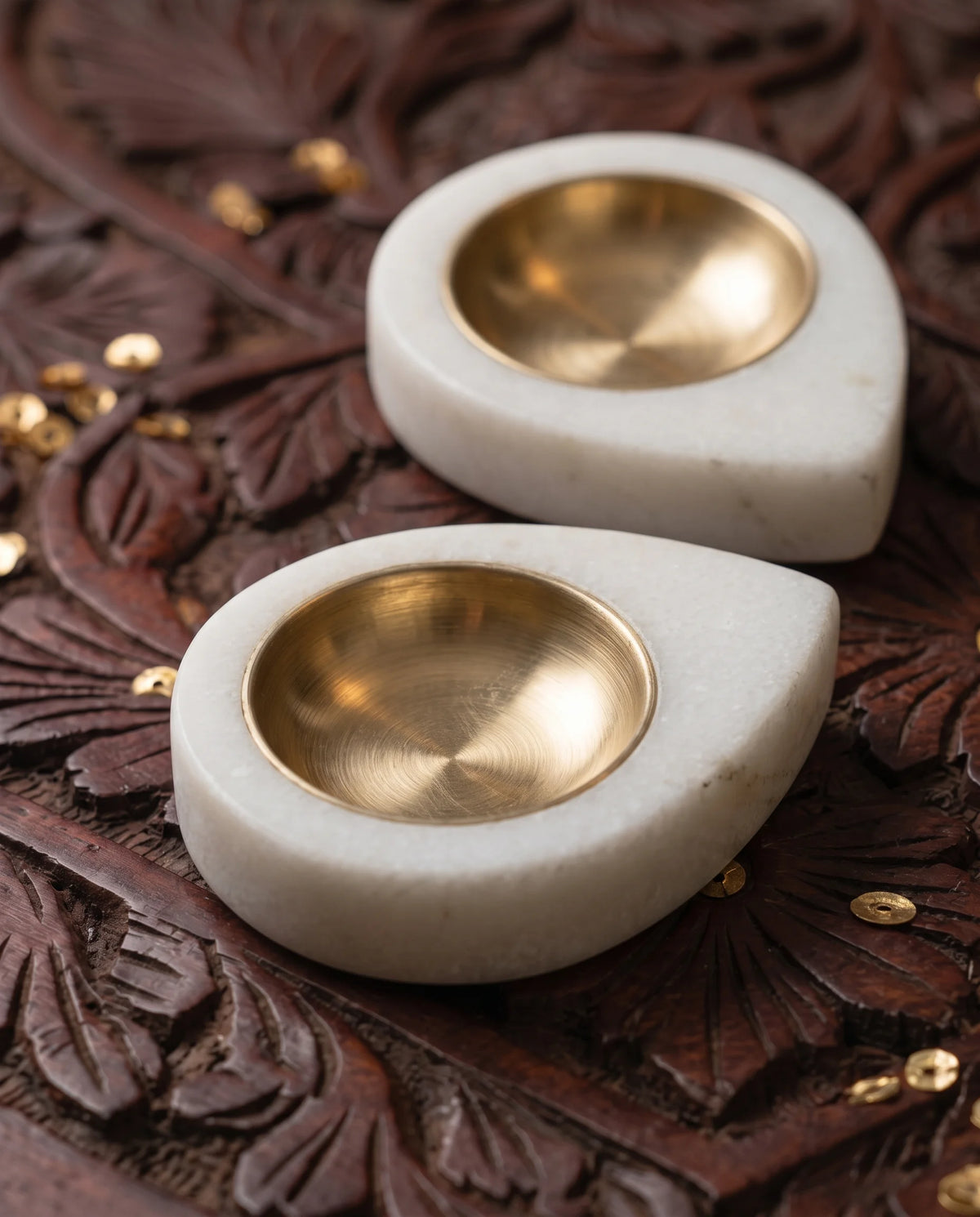 Close-up of white teardrop diya-holder bases surrounding round gold-tone cups.
