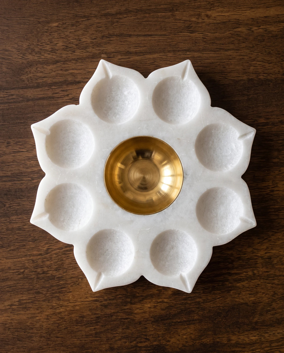 Overhead view of a white floral holder with a ring of lit recesses and a central gold-tone cup.