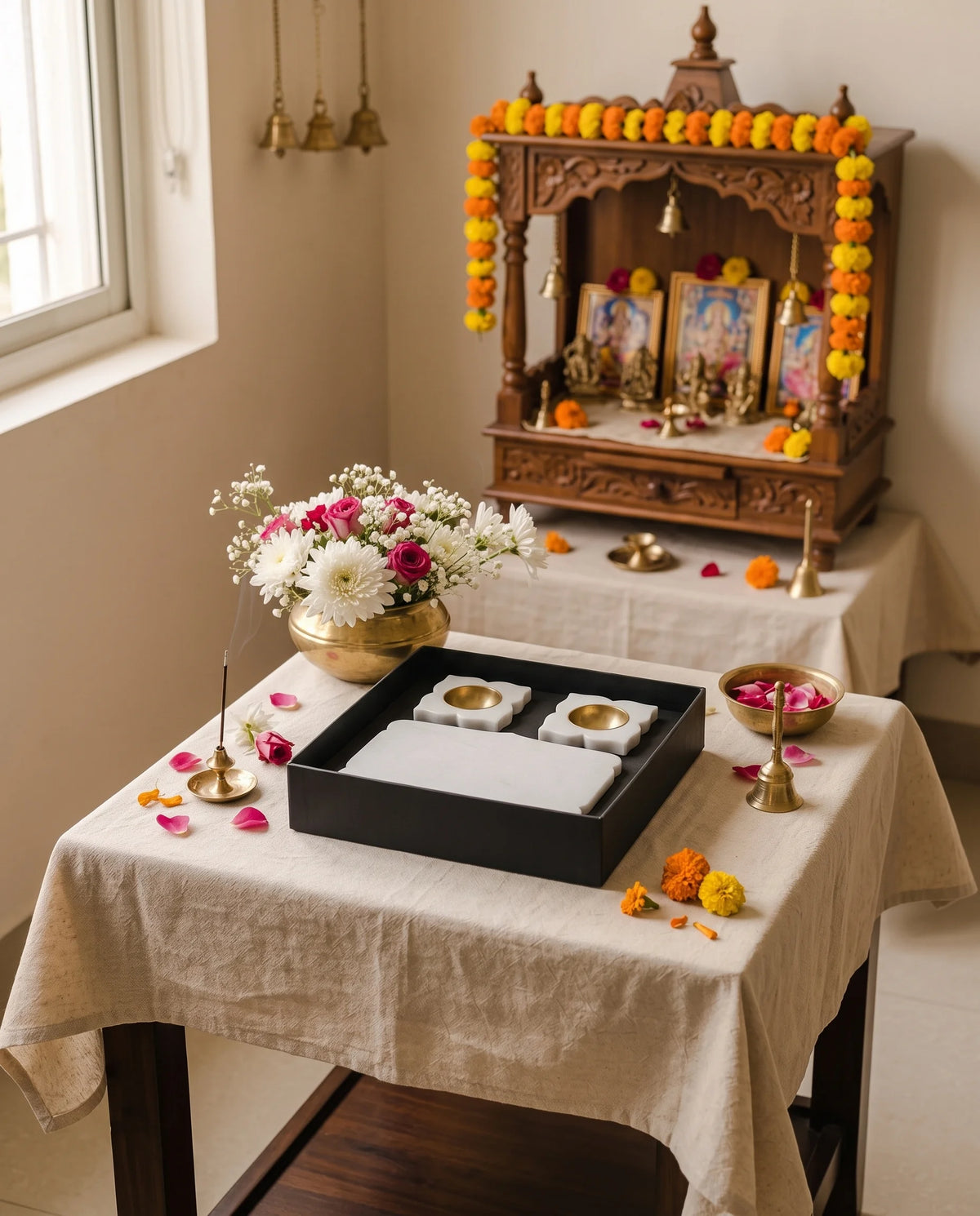 White pooja tray and holder designs in a black box styled on a table in front of a home altar.