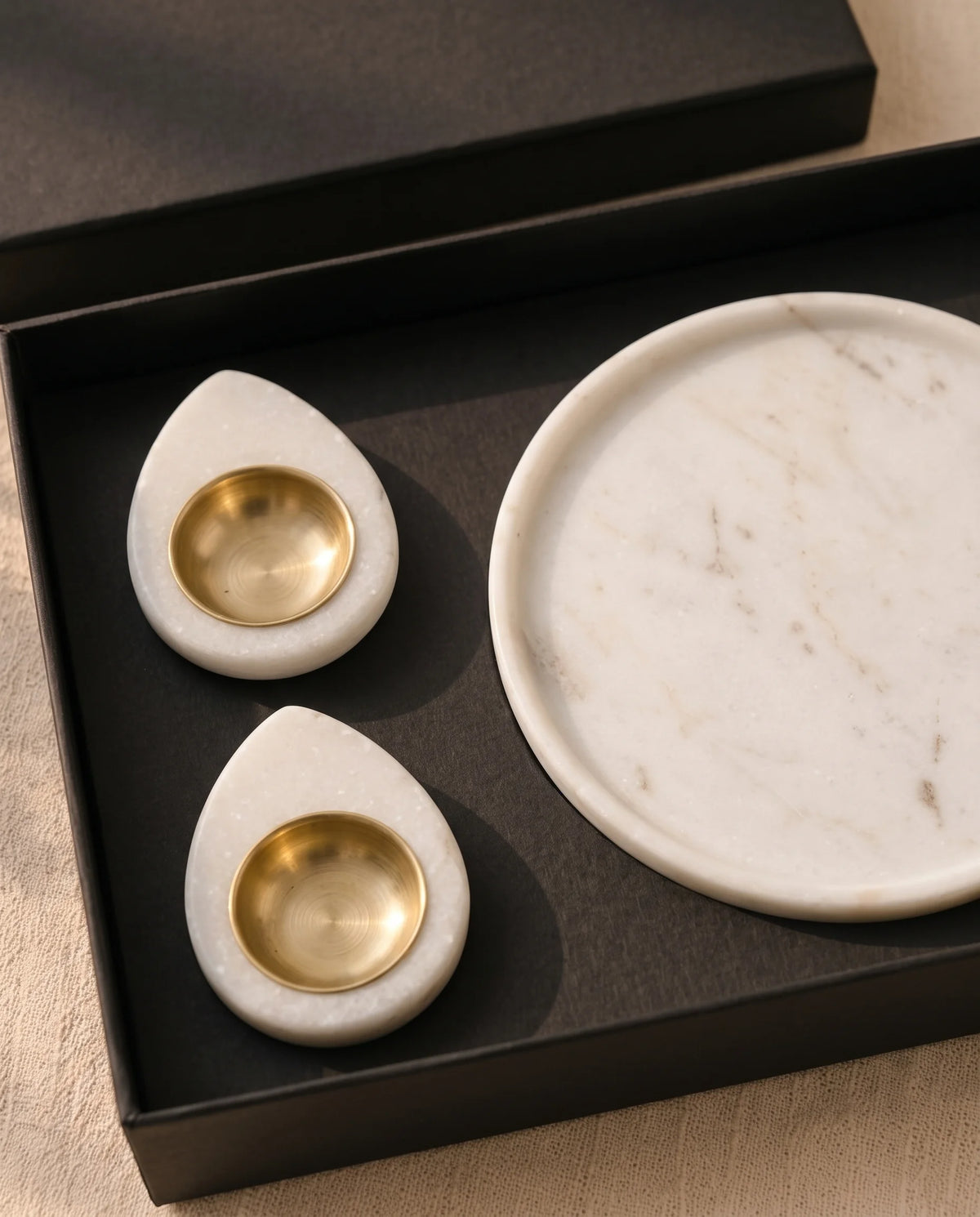 Overhead view of a white round dish and teardrop holder designs inside black presentation packaging.