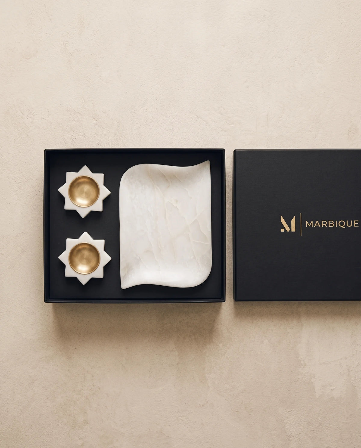 White scalloped tray and floral holders arranged inside open black Marbique packaging.