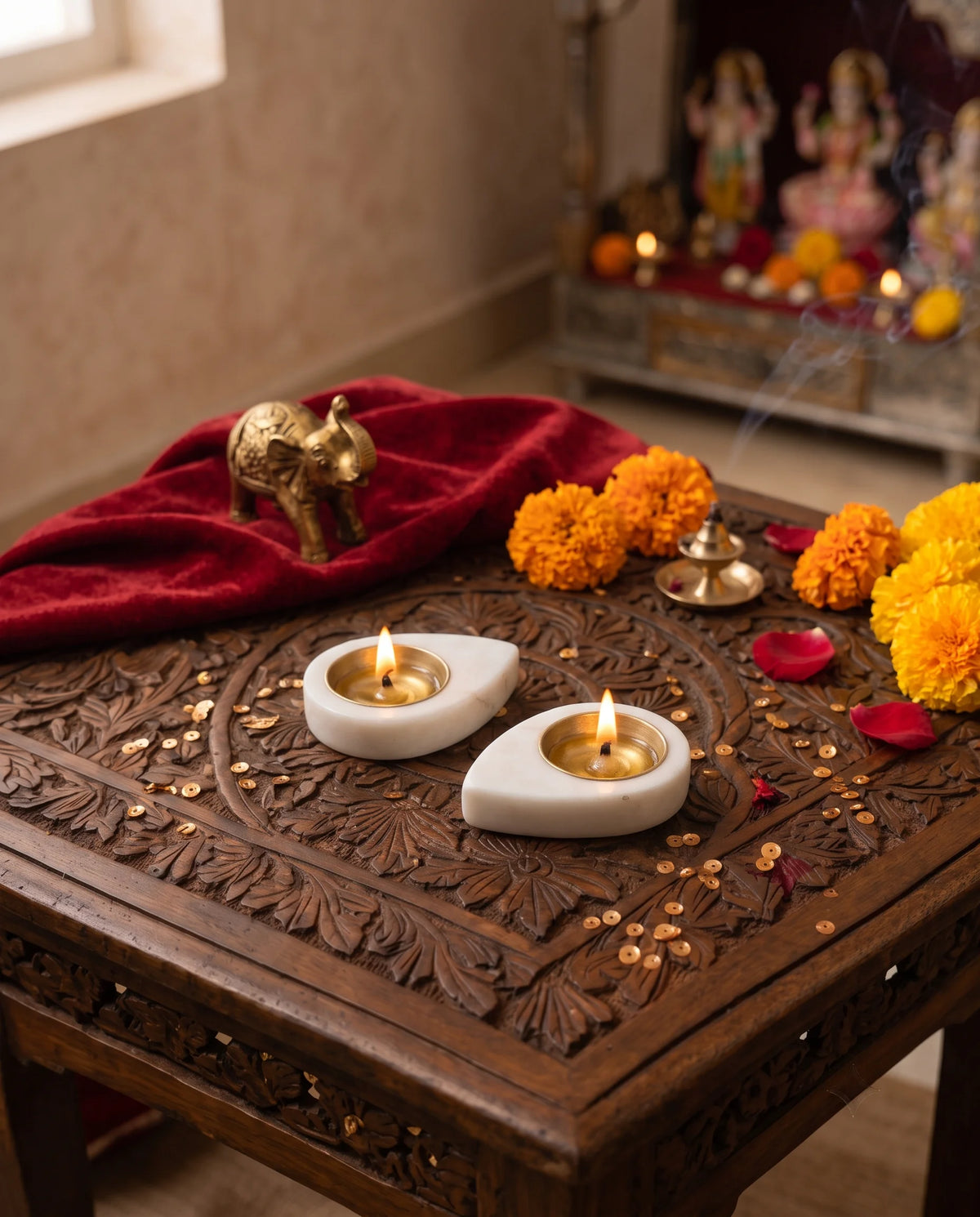 Two lit white teardrop diya holders styled with flowers and an elephant ornament in a pooja setting.
