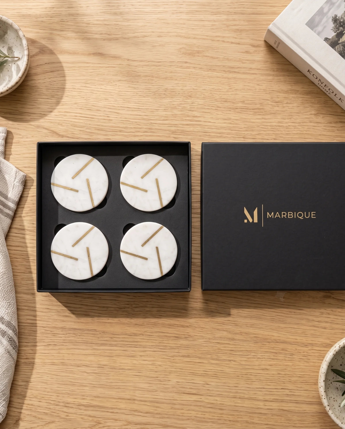 White circular coasters with gold-tone intersecting lines, with a hand holding a matching coaster.