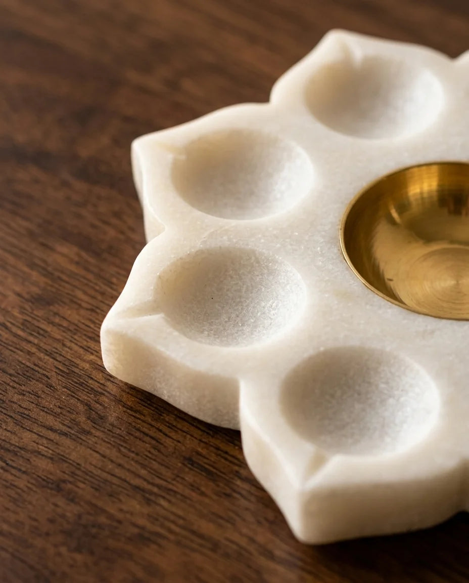 Unlit white flower-shaped holder with petal recesses and a gold-tone centre inside black Marbique packaging.