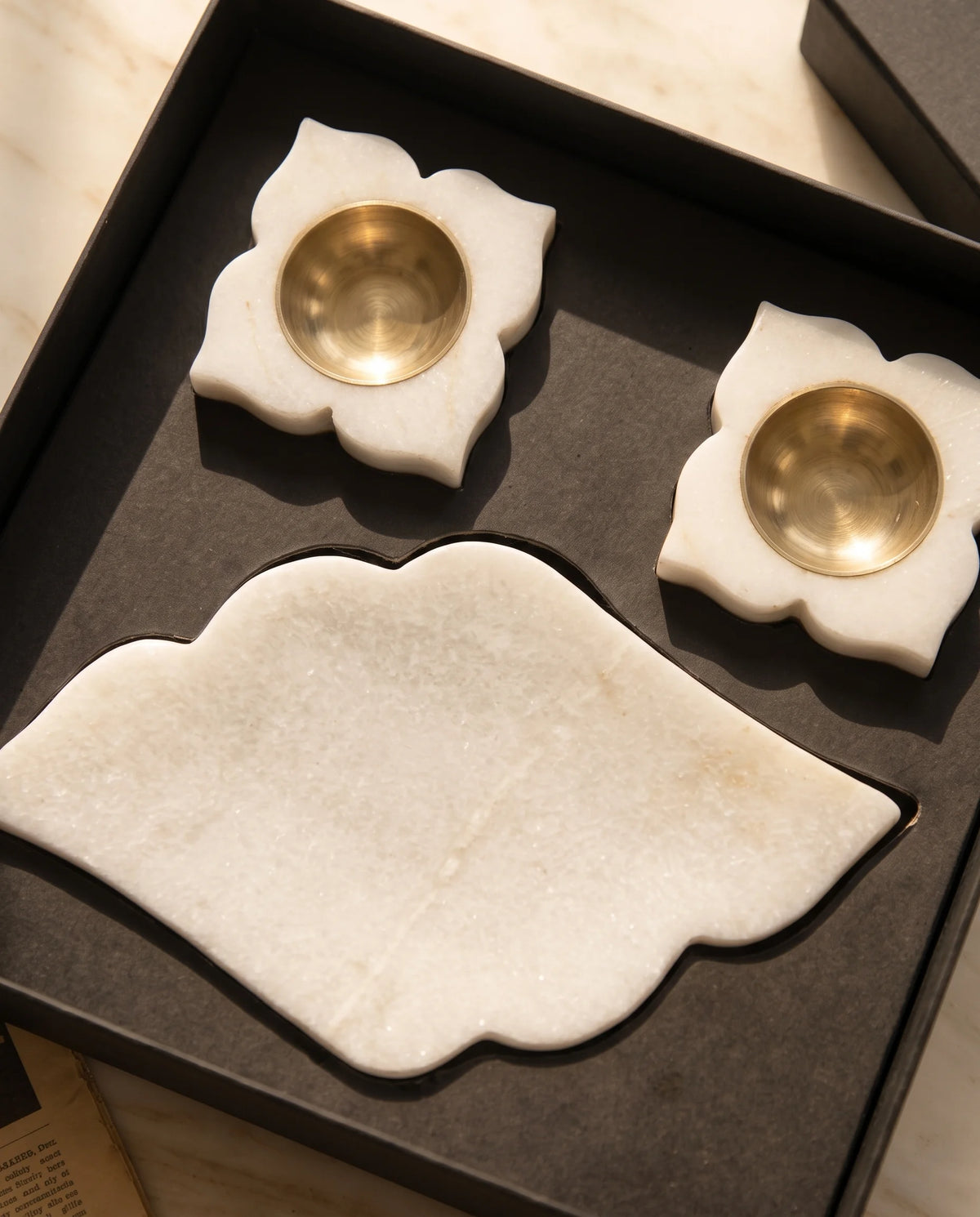Overhead view of the white pointed scalloped tray and floral holder designs in black packaging.