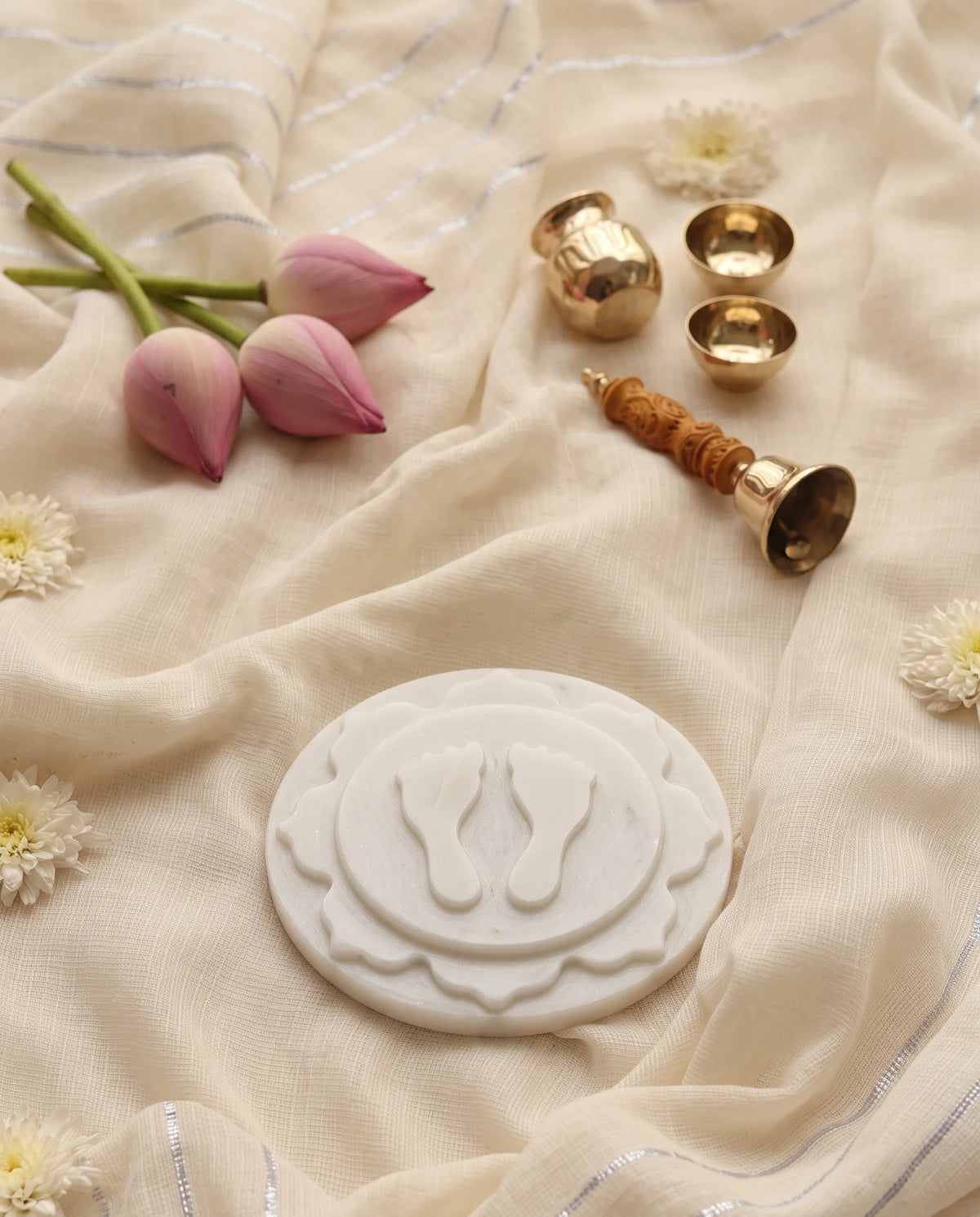 Angled view of the layered white footprint plaque beside a bell, vessels and pink lotus buds.