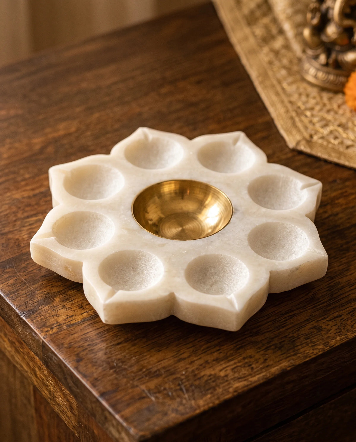 White floral holder with gold-tone centre styled with lit candles beside devotional decorations.