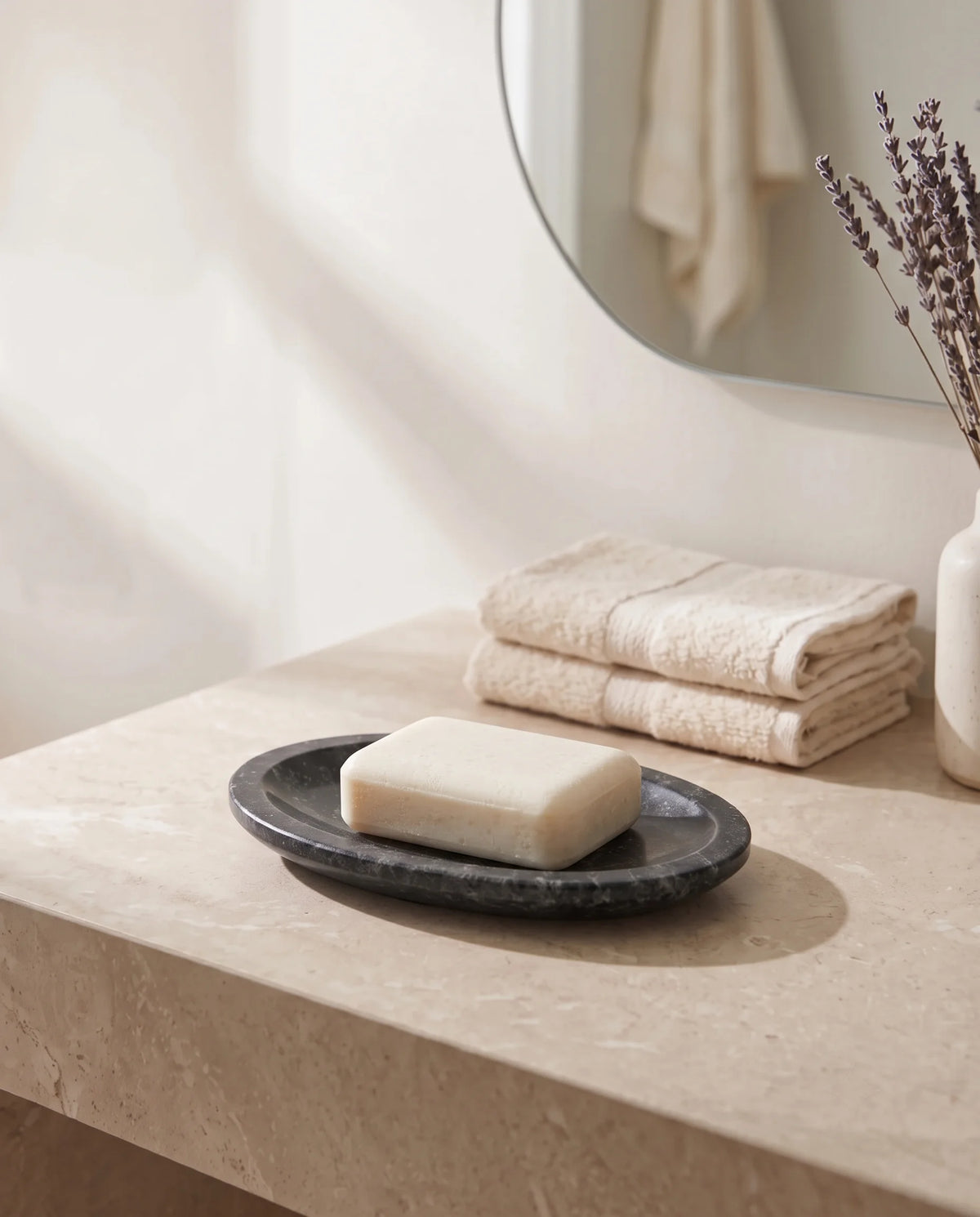Oval charcoal dish with pale veining, styled with a white bar of soap beside folded towels.