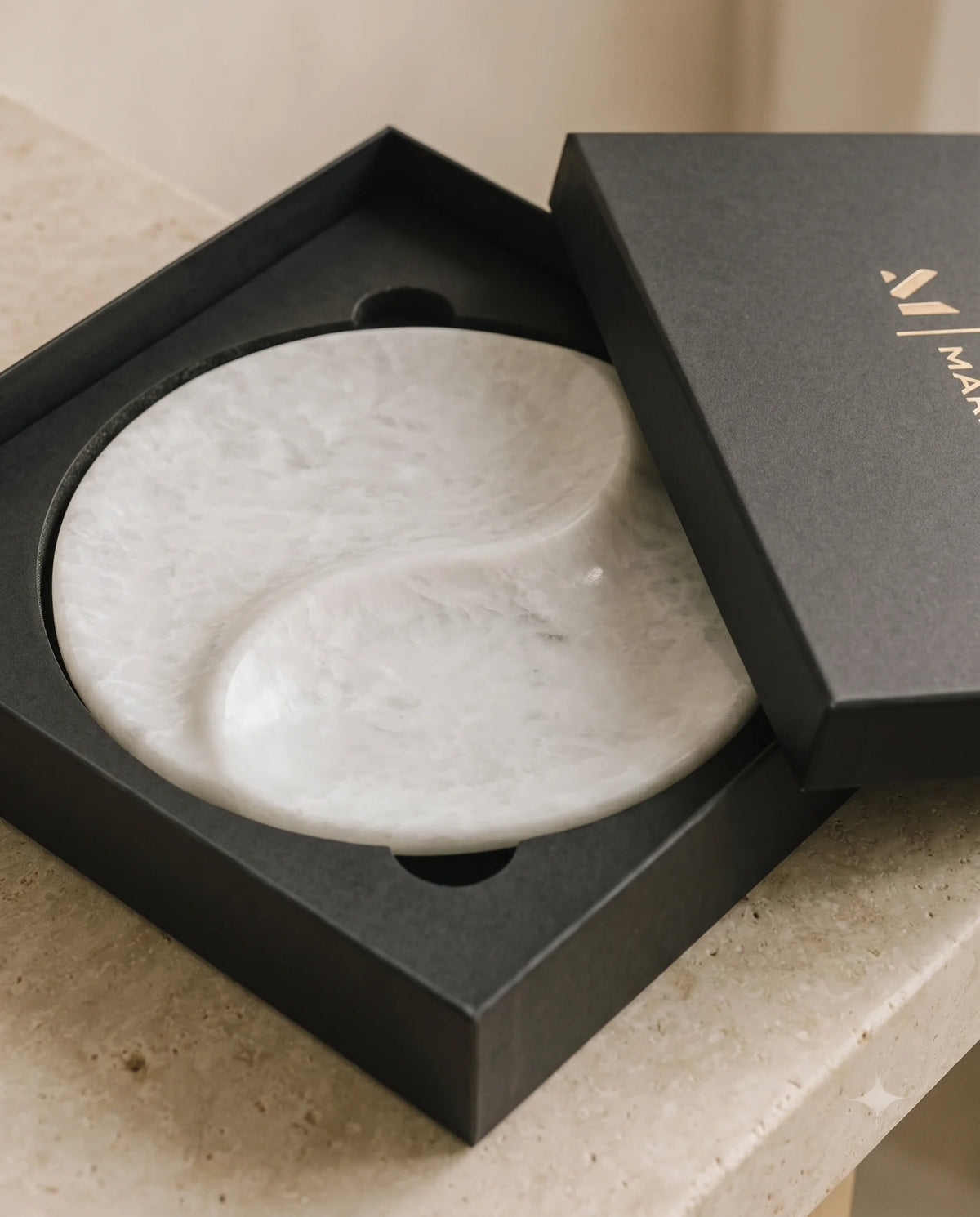 White round two-section tray with a curved divider inside partially open black Marbique packaging.