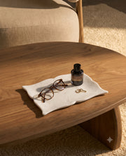 White pointed scalloped rectangular tray styled with glasses, a perfume bottle and keys on a wooden table.