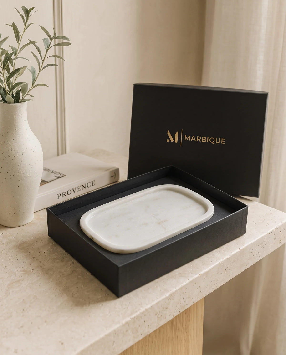 White rounded rectangular tray with a raised rim inside an open black Marbique box.