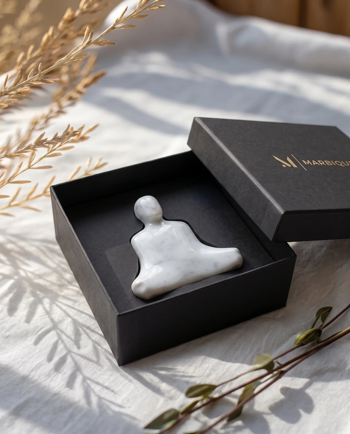 White seated-figure sculpture shown flat in a black Marbique presentation box.