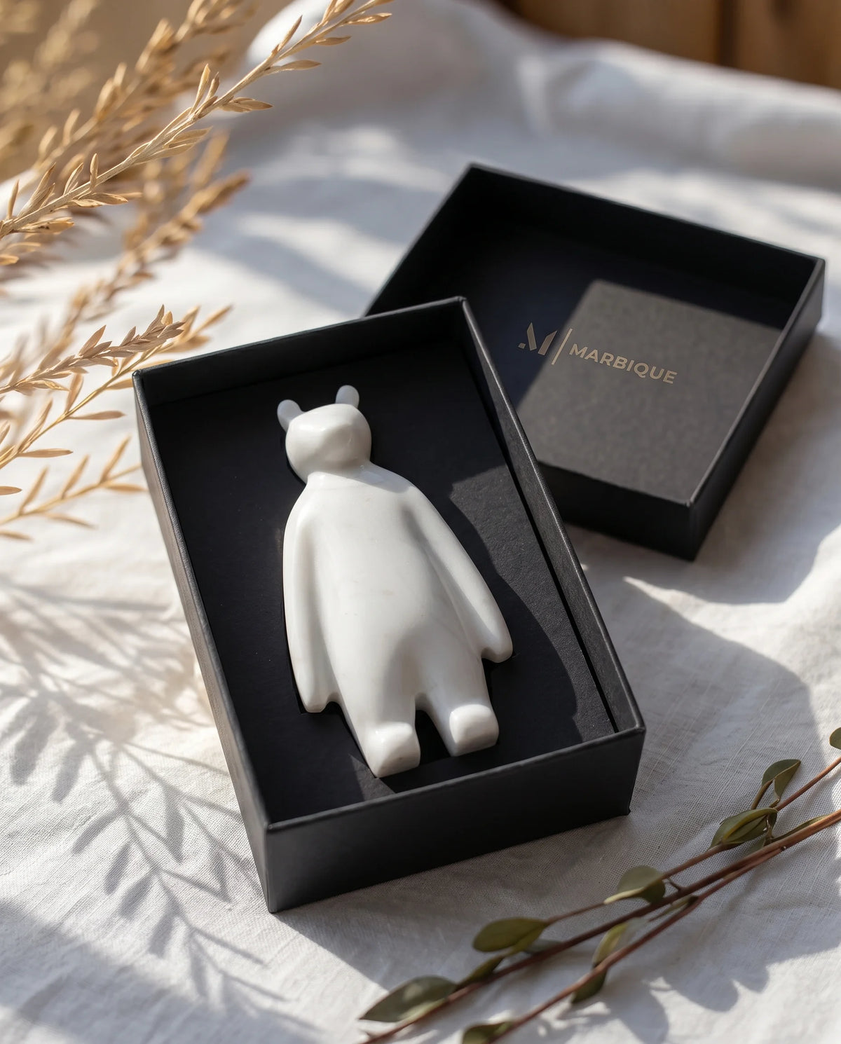White bear-like figure with separated feet displayed inside a black Marbique box.