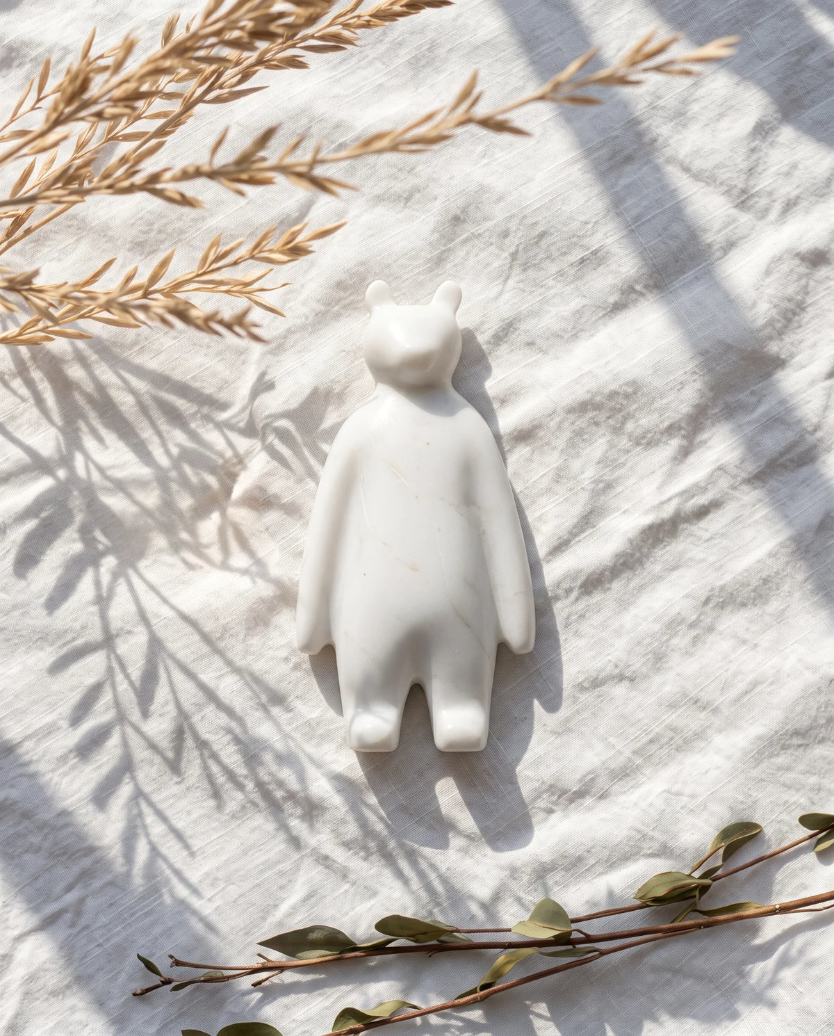 Overhead view of the white bear-like silhouette, rounded ears and elongated arms on light fabric.
