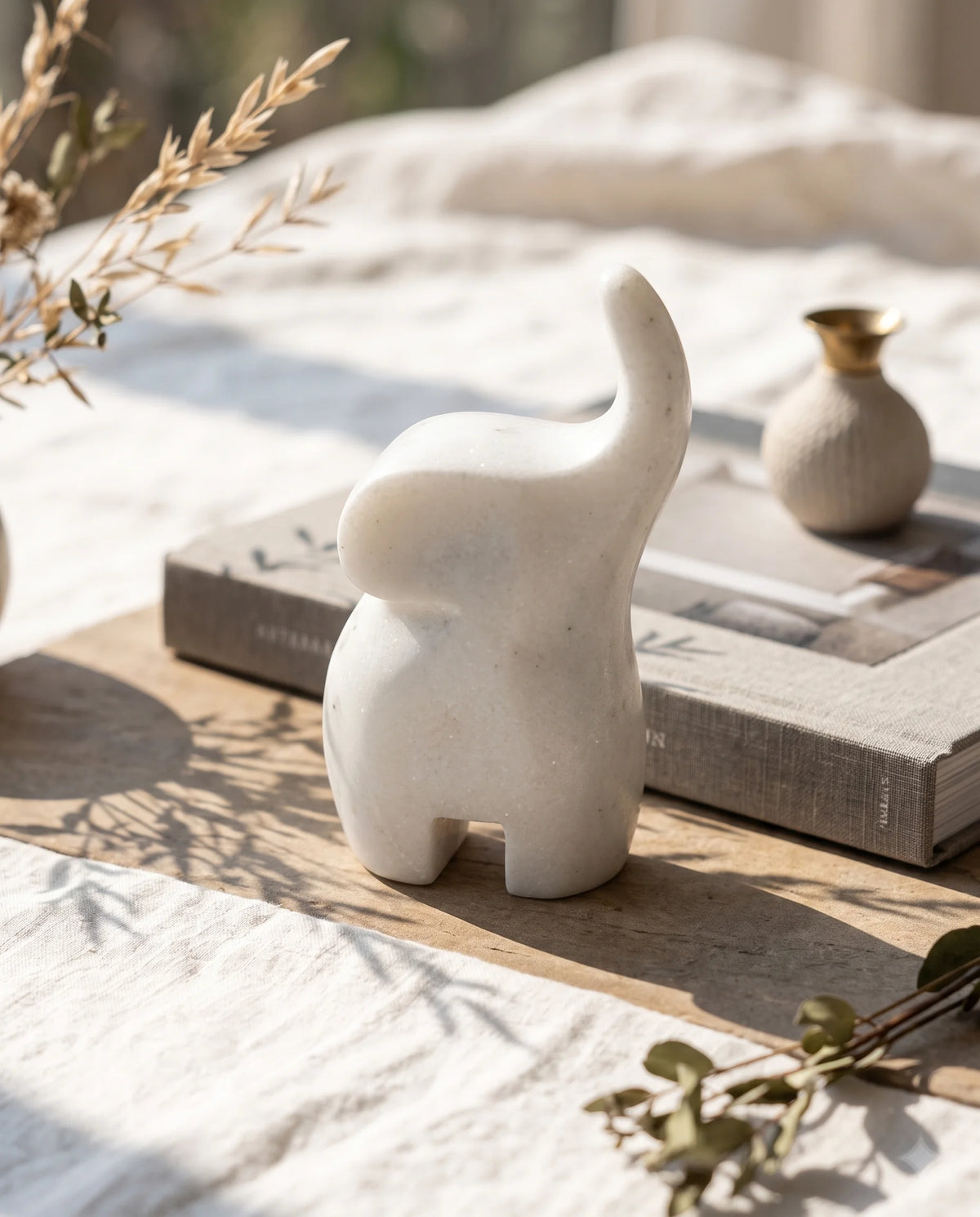 Upright white elephant with an upward-curving trunk styled beside a book and small vase.