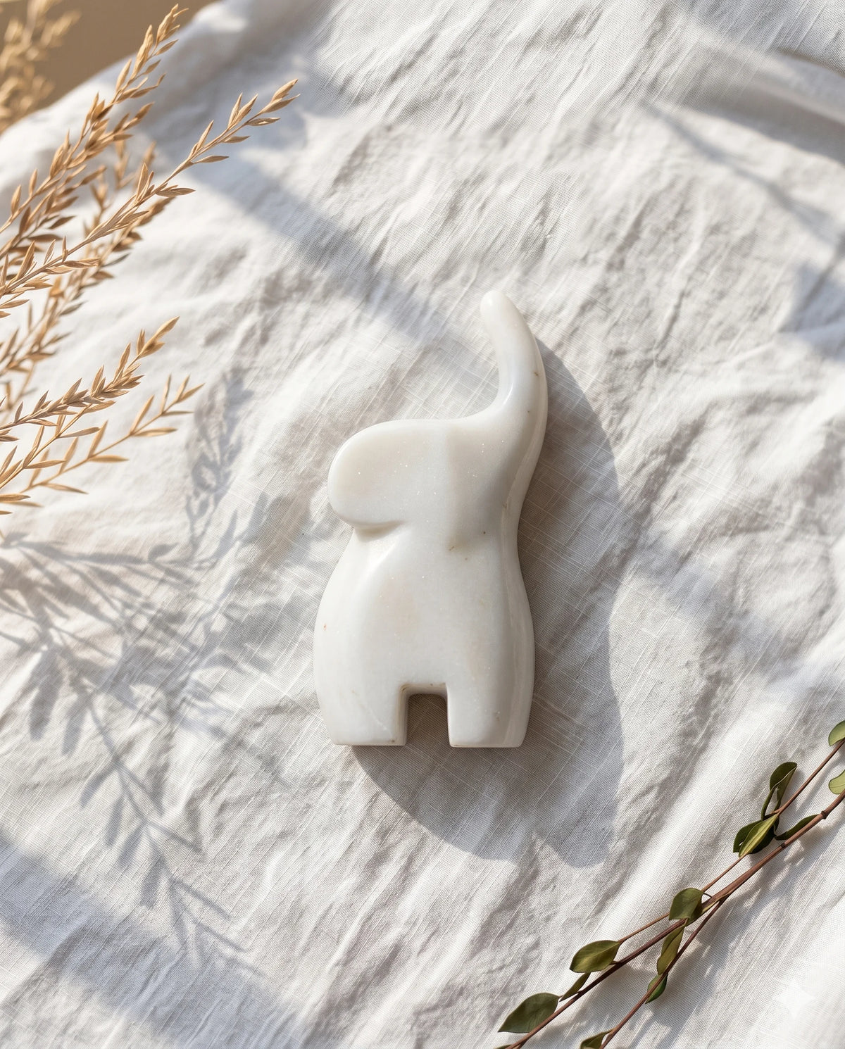 Overhead view of the white elephant form and raised trunk on light fabric.