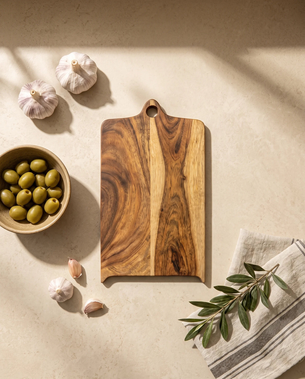 Overhead view of the brown shaped rectangular board with circular handle hole beside garlic and olives.