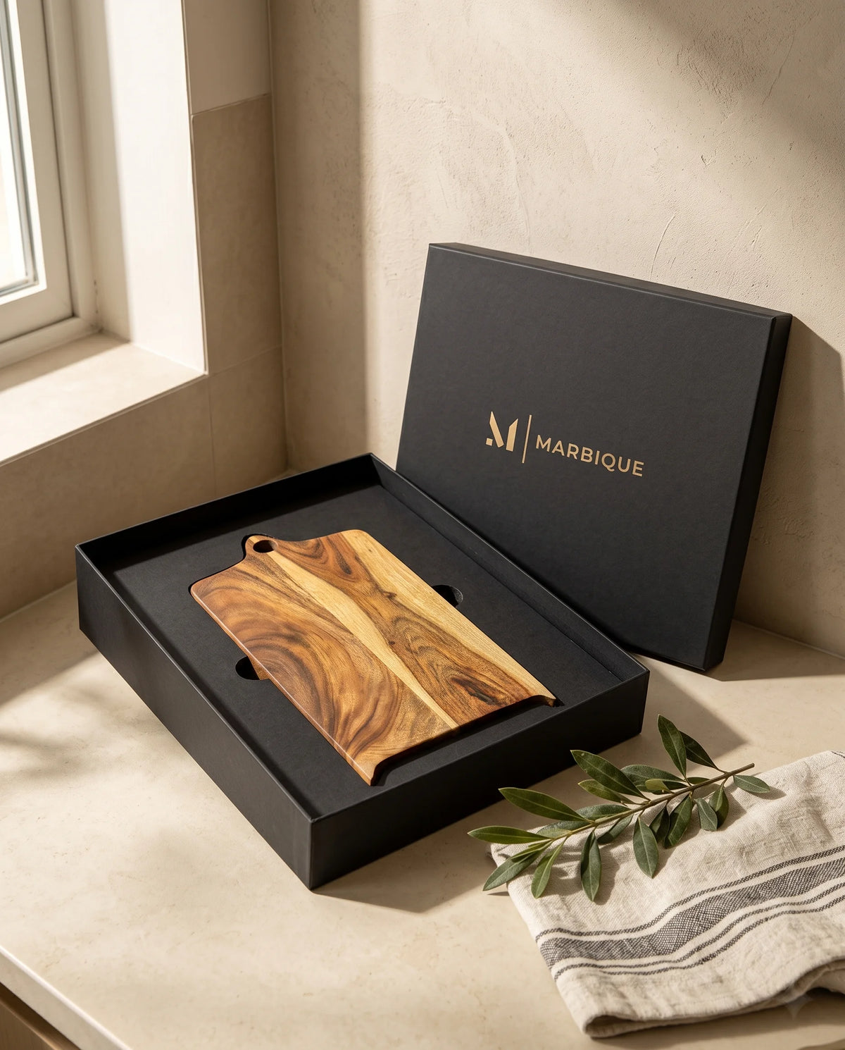 Brown shaped board displayed in a black Marbique box beside folded fabric and leaves.