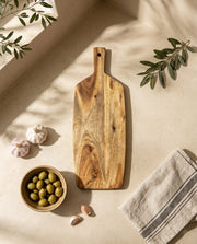 Overhead view of the brown paddle board and small handle hole beside garlic and olives.