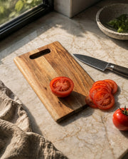 Brown rectangular board with a slotted grip, styled with sliced tomatoes beside a knife.